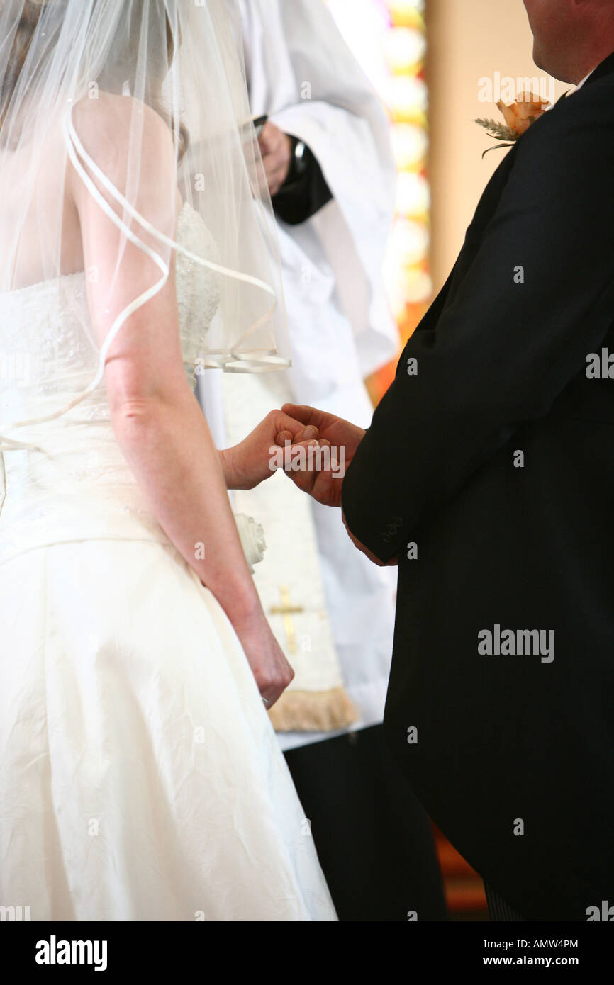 Sposa e lo sposo tenendo le mani durante il servizio di nozze (da dietro) con il vicario nella parte anteriore Foto Stock