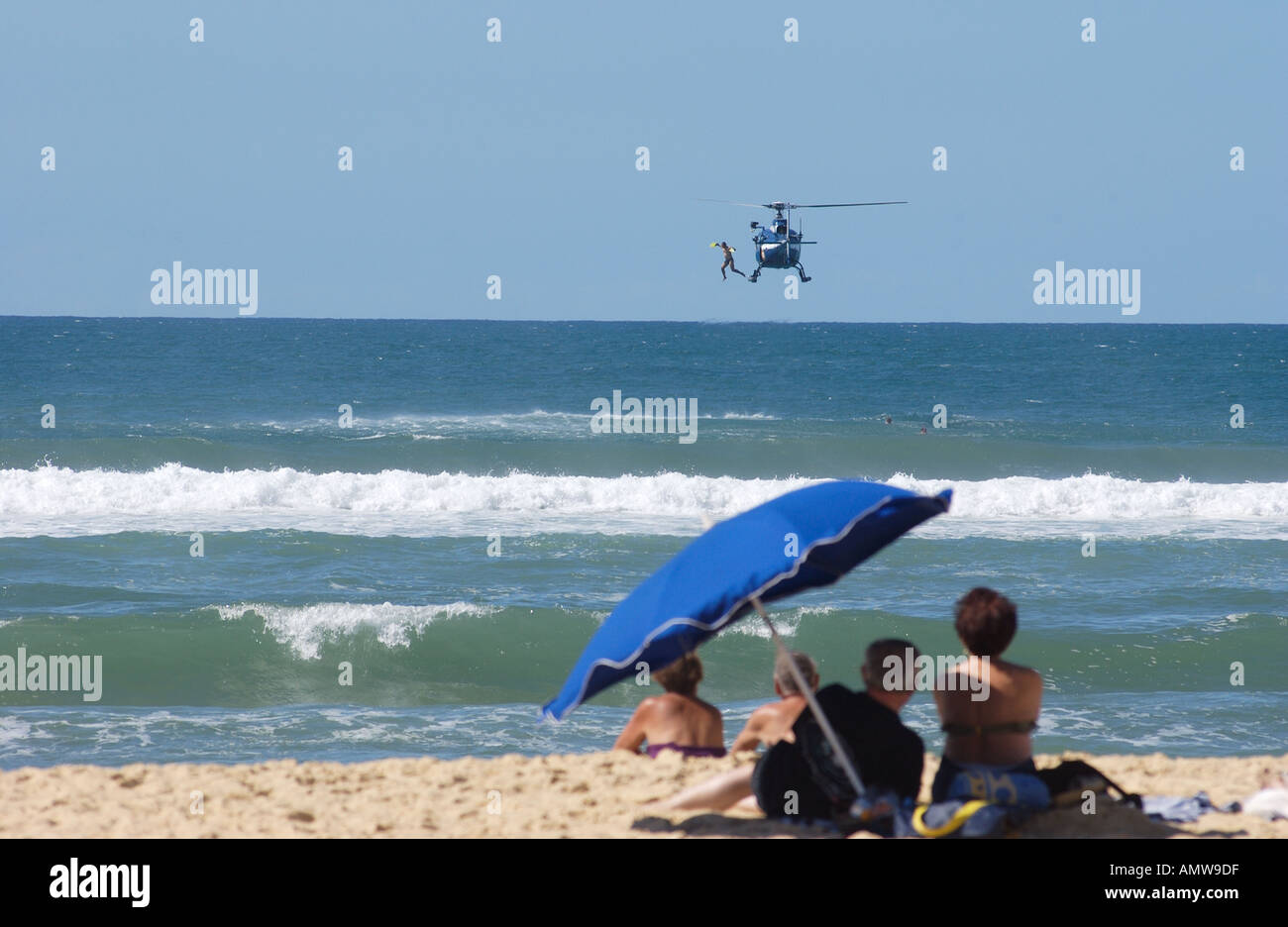 Elicottero francese per il salvataggio aereo in mare che fa cadere un bagnino nel mare. I villeggianti guardano sulla spiaggia da sotto un ombrellone. Messange spiaggia Francia Foto Stock
