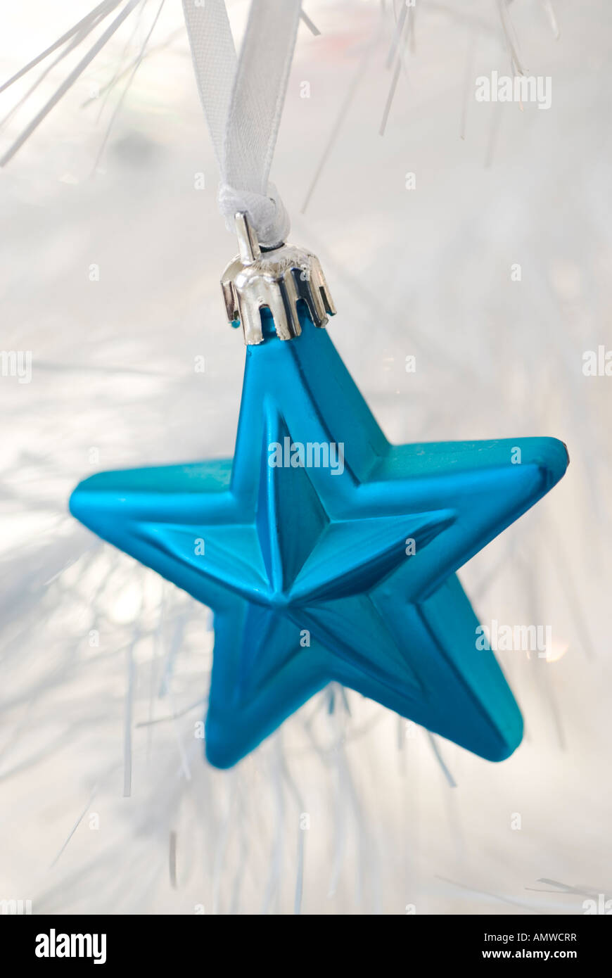 Un blue star holiday ornamento appeso a un bianco albero di Natale artificiale. Foto Stock