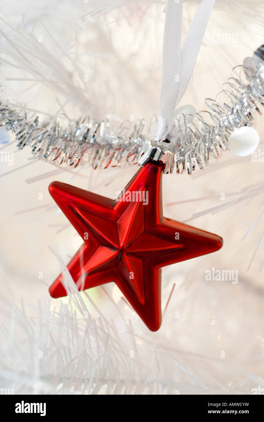 Una stella rossa holiday ornamento appeso a un bianco albero di Natale artificiale. Foto Stock
