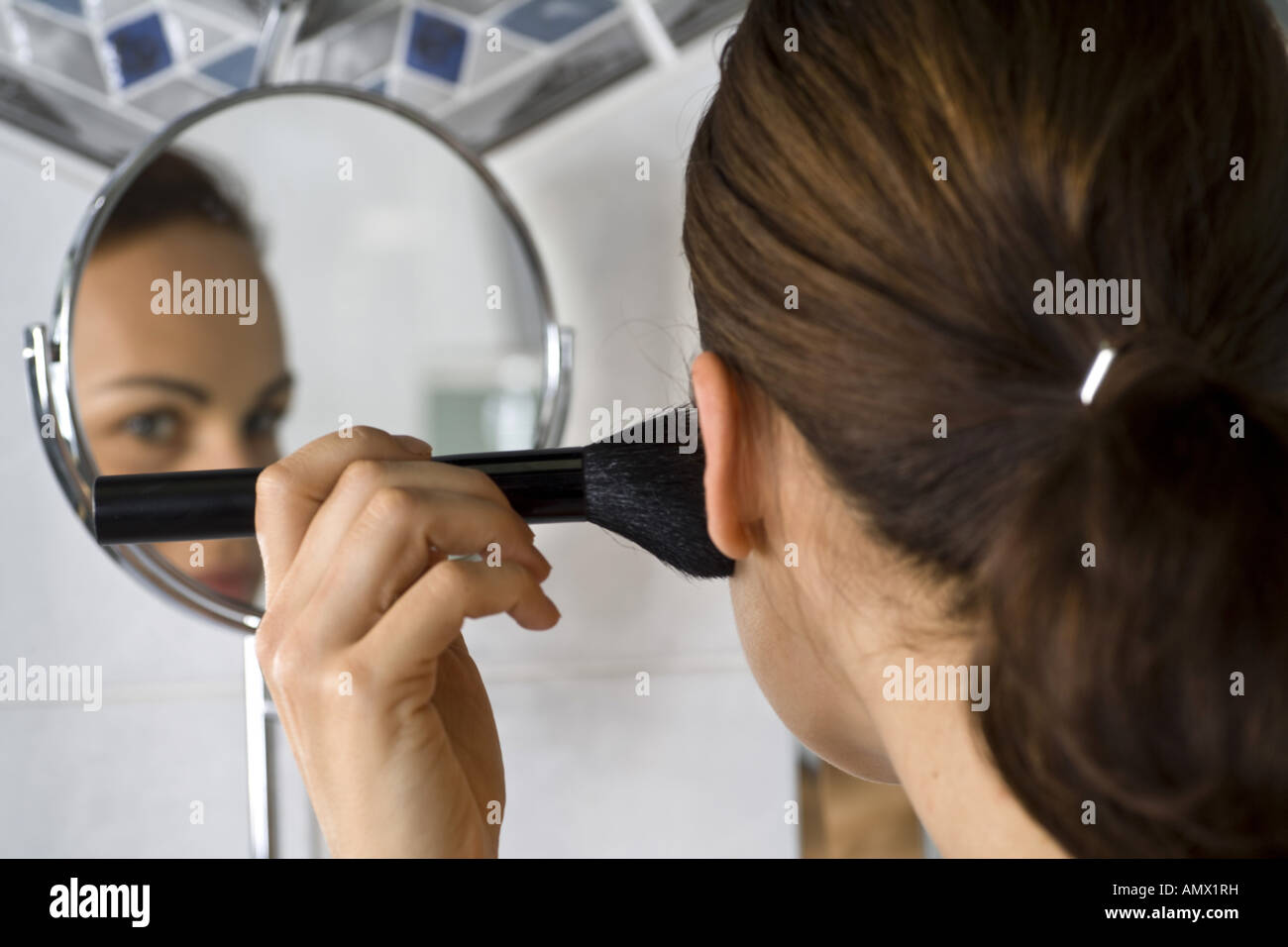 Giovane donna puttin sul trucco nella parte anteriore di uno specchio Foto Stock