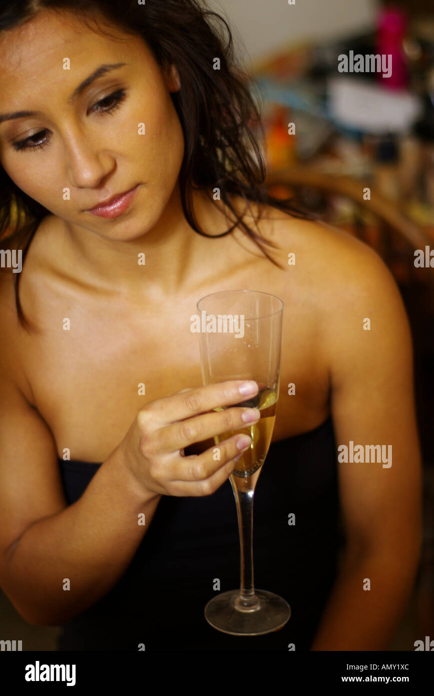 Una giovane donna sta tenendo in mano un bicchiere di vino bianco e di bere cercando molto solitaria Foto Stock