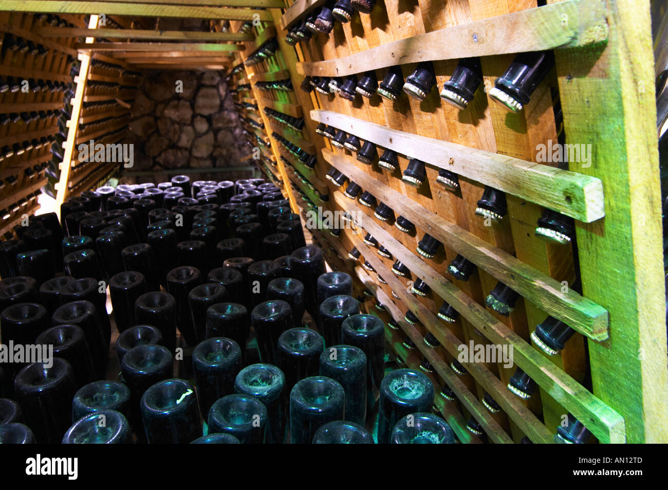 Bottiglie per vino spumante in piedi a testa in giù in una sorta di  pupitres cesti da tavolozze. Altre bottiglie in rack tradizionali. mostra i  tappi a corona. Vita@I Vitaai Vitai Gangas