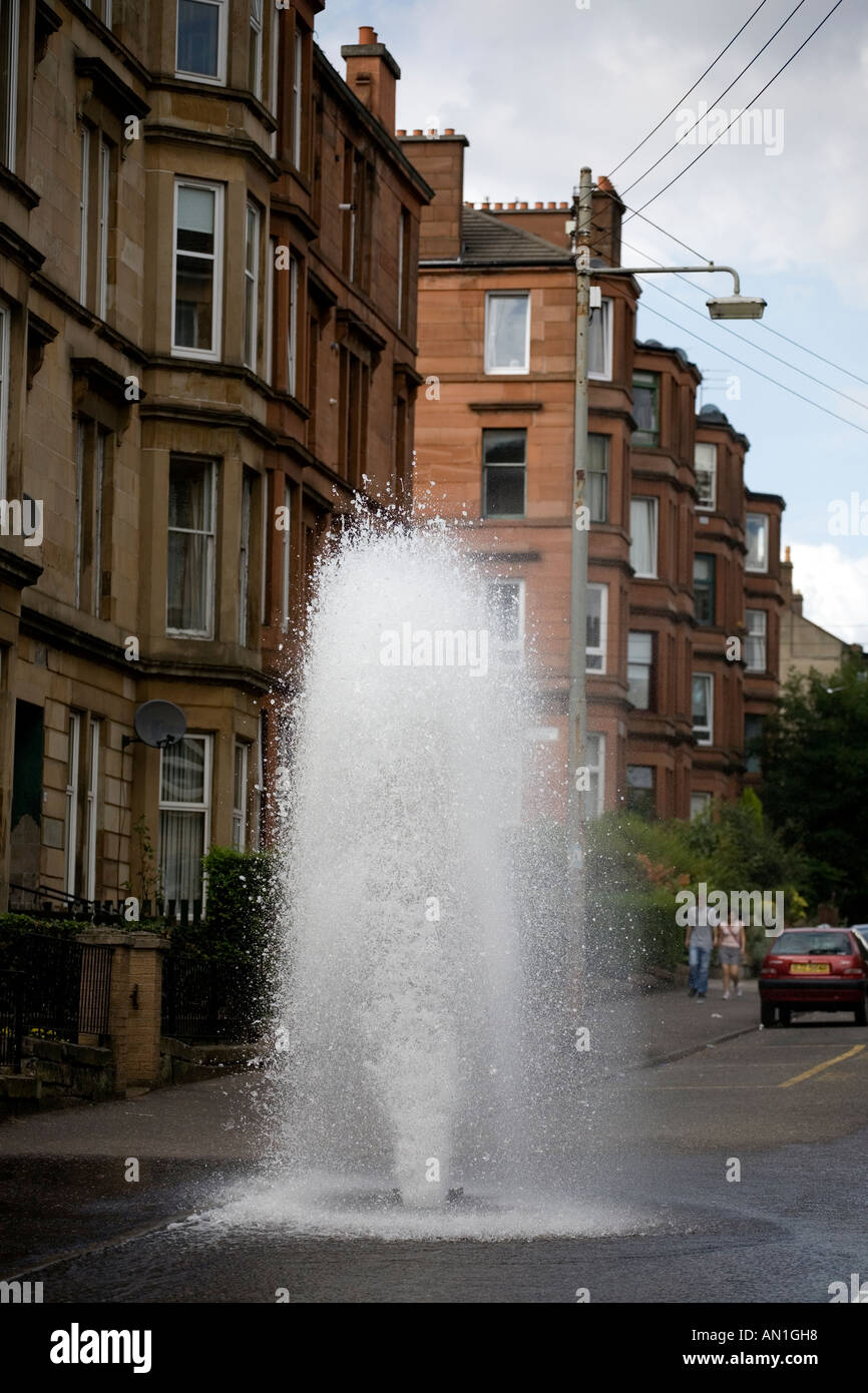 Un acqua principale idrante a burst e sgorga un acqua in una strada di Dennistoun Glasgow REGNO UNITO Foto Stock