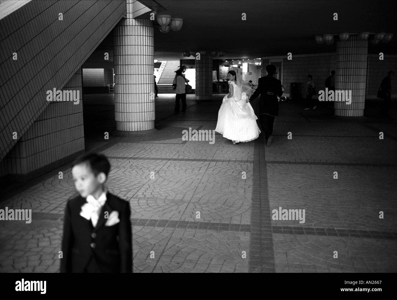 Nel cuore di Hong Kong, in Cina, una sposa gioiosa corre mentre un ragazzo di pagina si trova in primo piano. Foto Stock