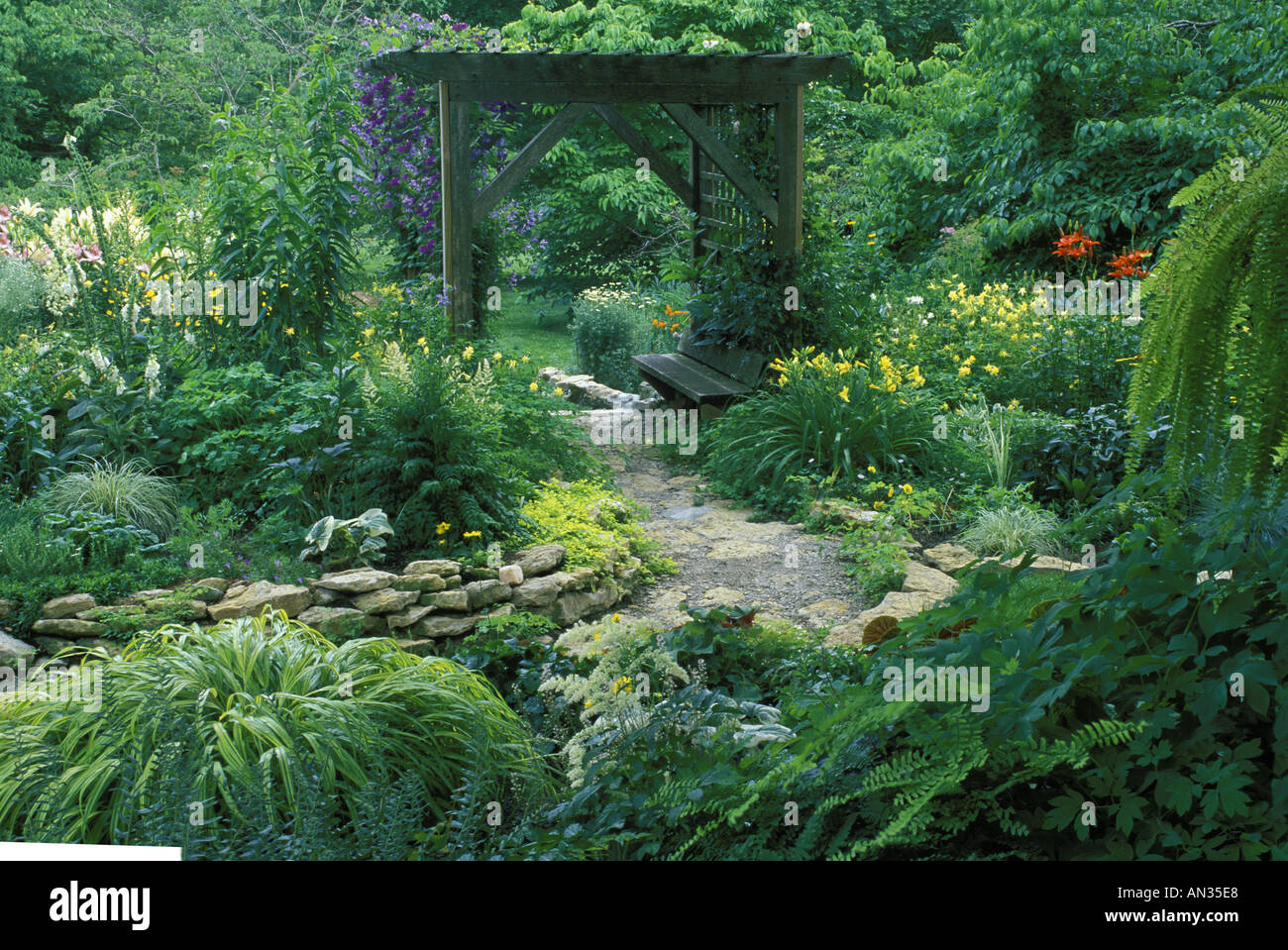 Tranquillo: Un sentiero flagstone con muro di pietra in giardino privato giardino fiorito cortile conduce attraverso un albero di legno con sede Missouri Stati Uniti Foto Stock
