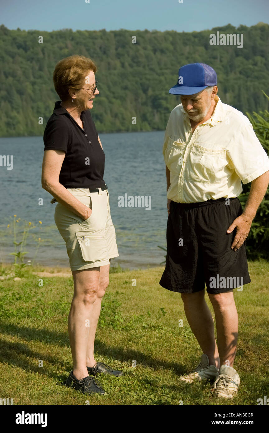 Gli anziani uomo e donna con le discussioni sulla spiaggia accanto a un lago blu Foto Stock