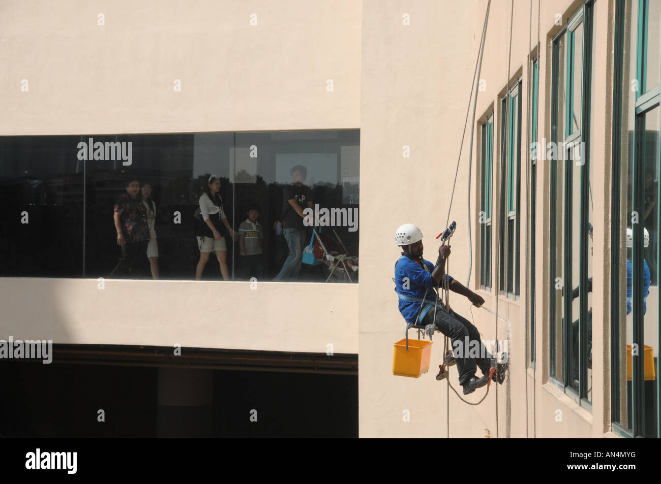 Un detergente per vetri al lavoro mentre i pedoni a piedi attraverso un passaggio pedonale al Sunway Lagoon, Malaysia Foto Stock