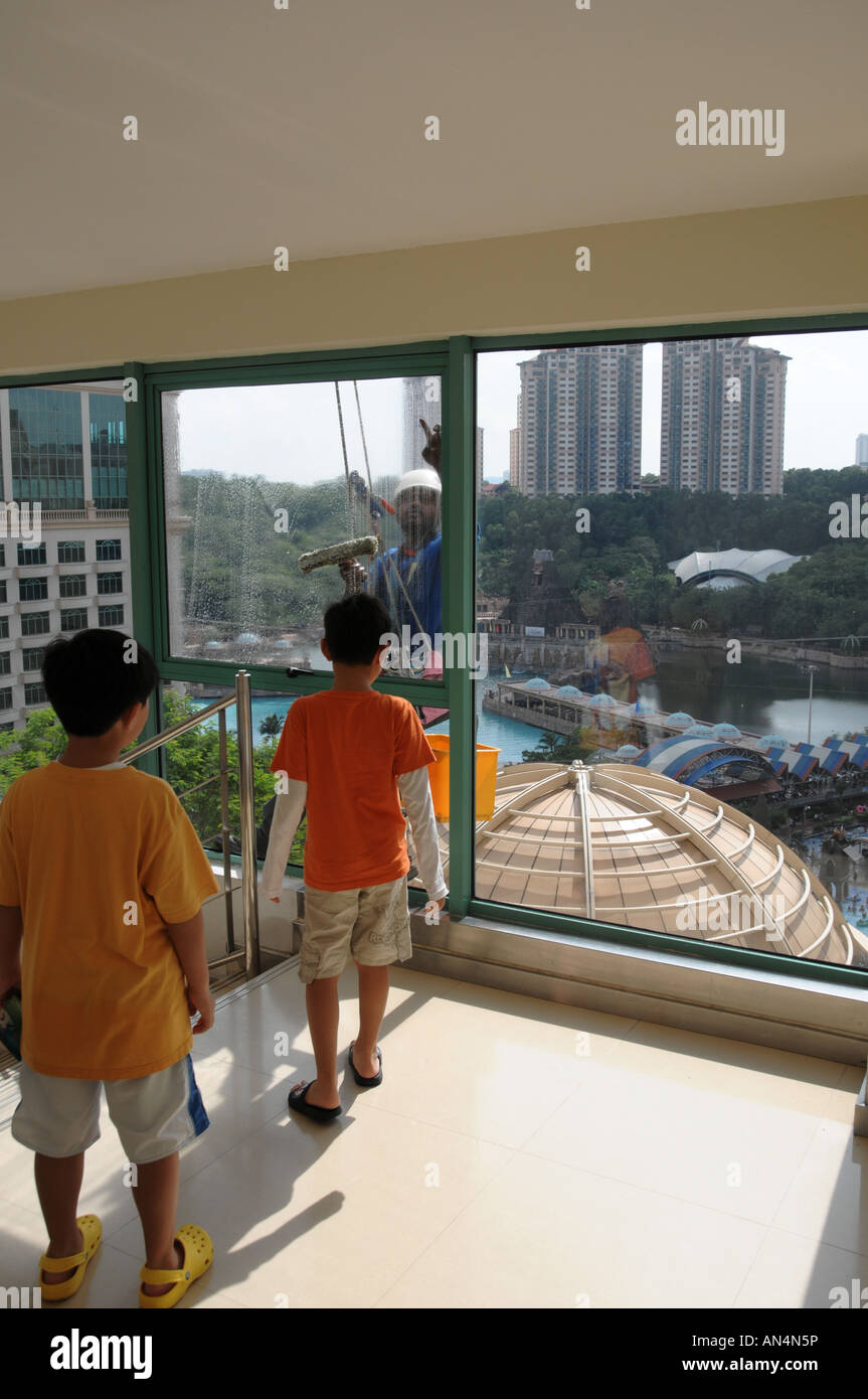 Due bambini guardando un detergente per vetri al lavoro per la pulizia del vetro esterno di un complesso di negozi in Sunway Lagoon, Malaysia Foto Stock