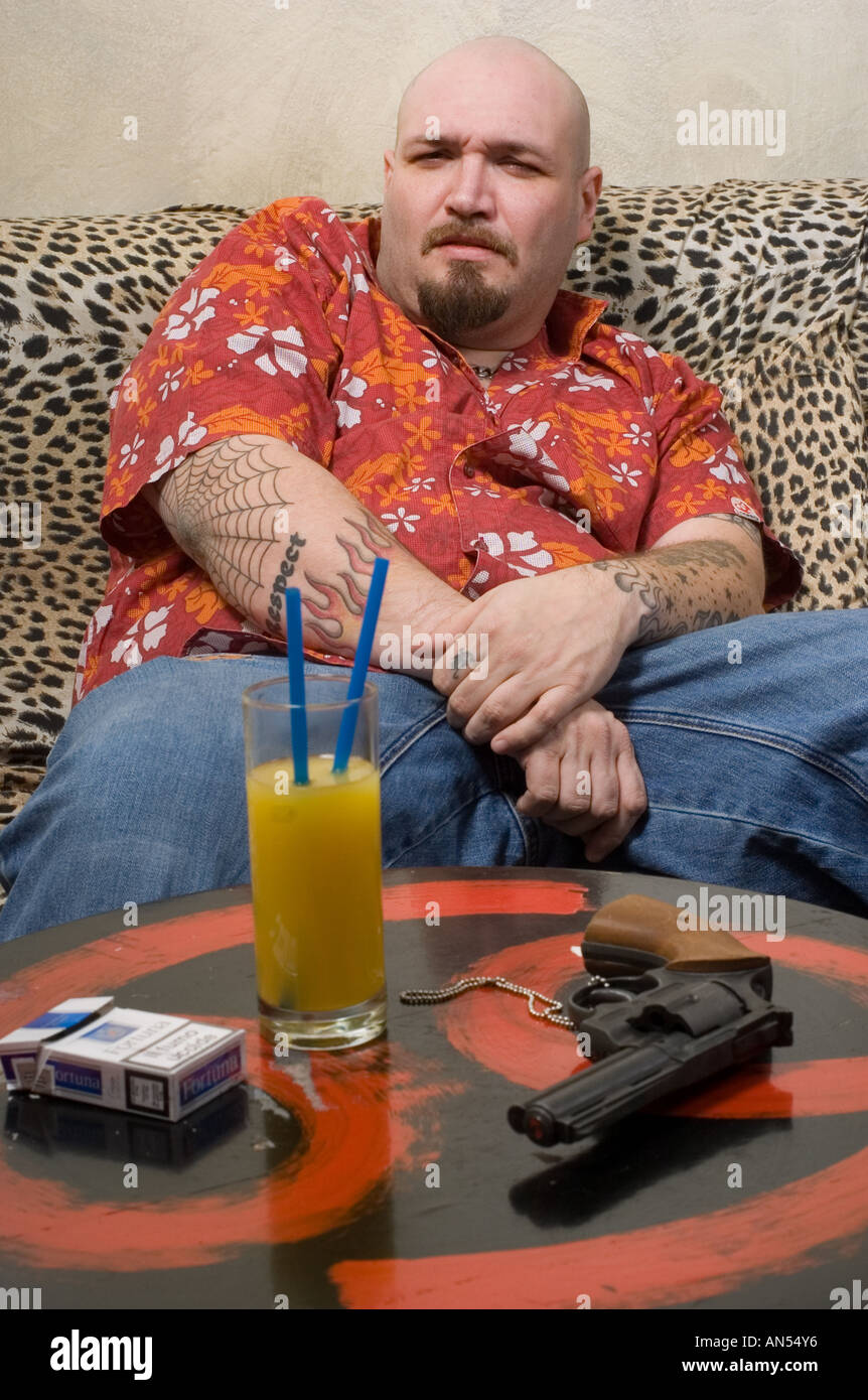Fat Man in maglietta arancione su leopard lettino con pistola e bere grinning Foto Stock