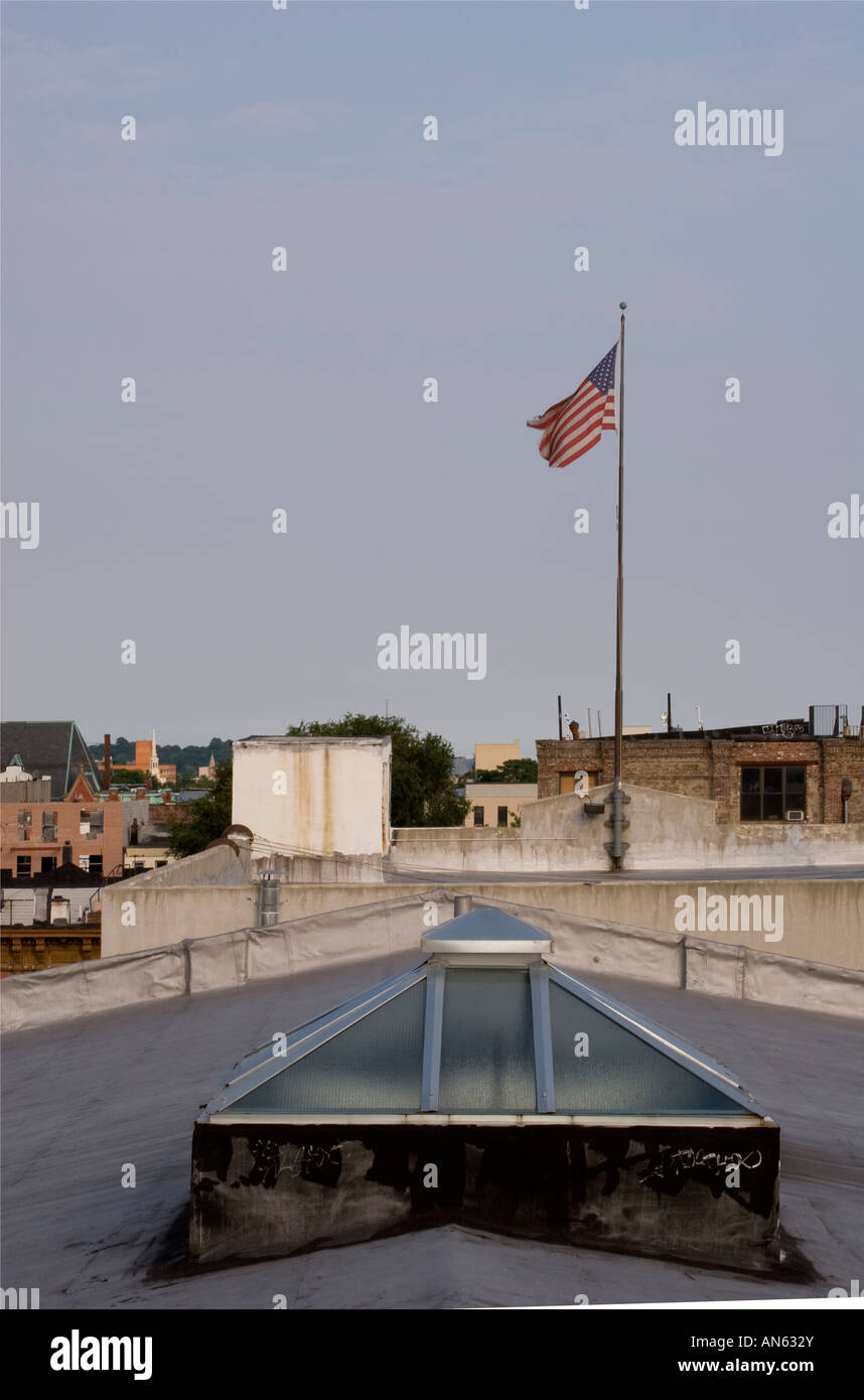 Una bandiera americana che sventola sopra un vecchio tetto di un magazzino a Brooklyn, New York, con edifici industriali sullo sfondo. Foto Stock