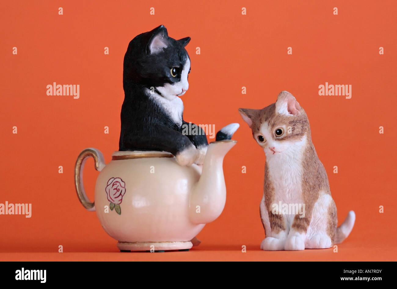 Modelli di ceramica di due gattini. Uno in una teiera con coda sporgente del tubo di lancio e gli altri a guardare Foto Stock
