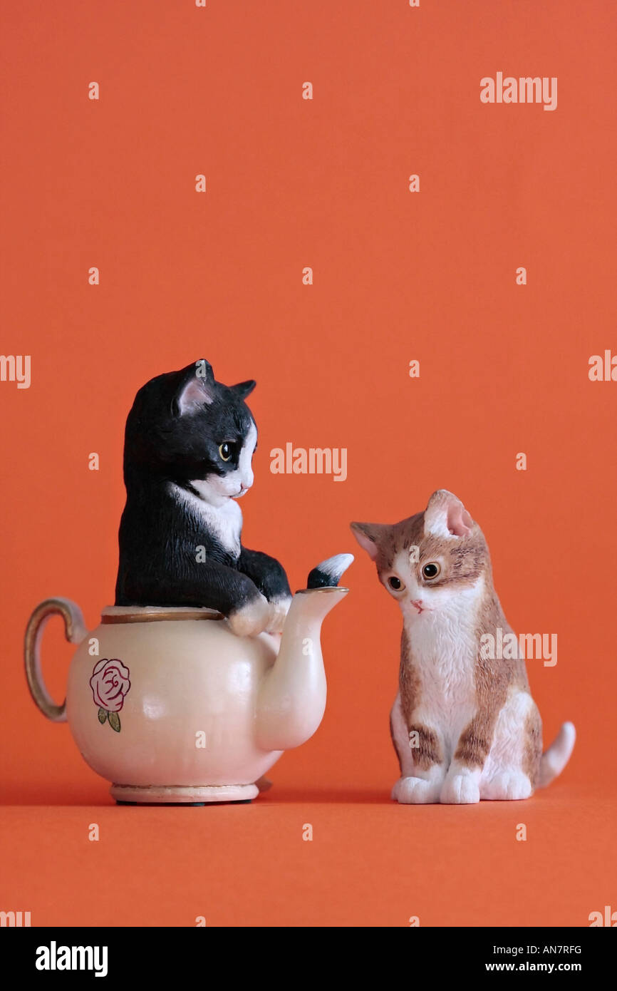 Modelli di ceramica di due gattini. Uno in una teiera con coda sporgente del tubo di lancio e gli altri a guardare Foto Stock