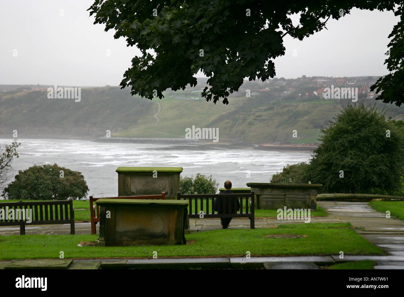 Uomo seduto sul sedile nella chiesa cimitero affacciato sul South Bay a Scarborough North Yorkshire Foto Stock