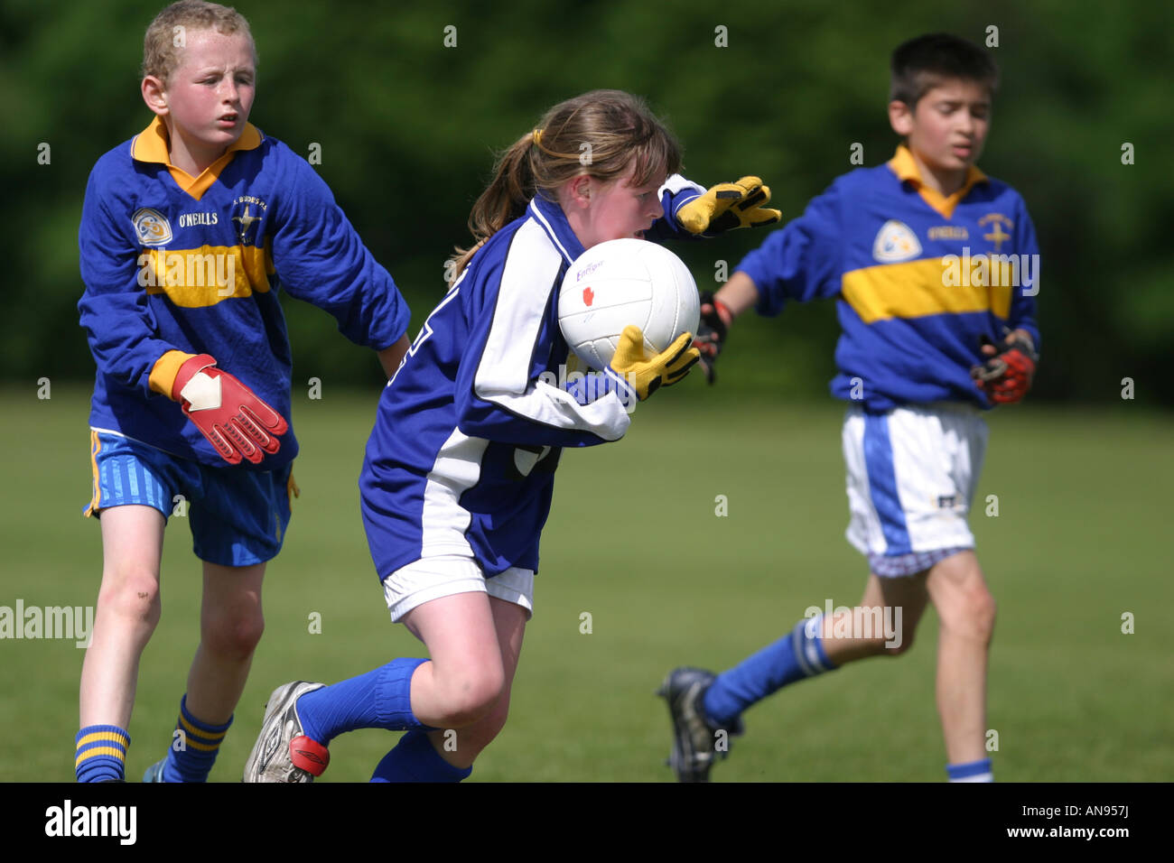 Ragazza giovane affronta due giovani ragazzi durante juniort calcio gaelico gioco in Belfast Foto Stock