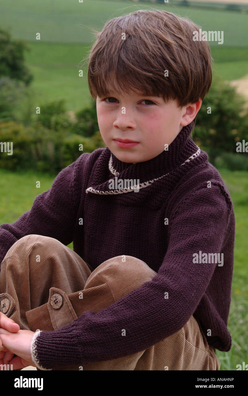 Ritratto di un giovane ragazzo seduto fuori cercando grumpy Foto Stock