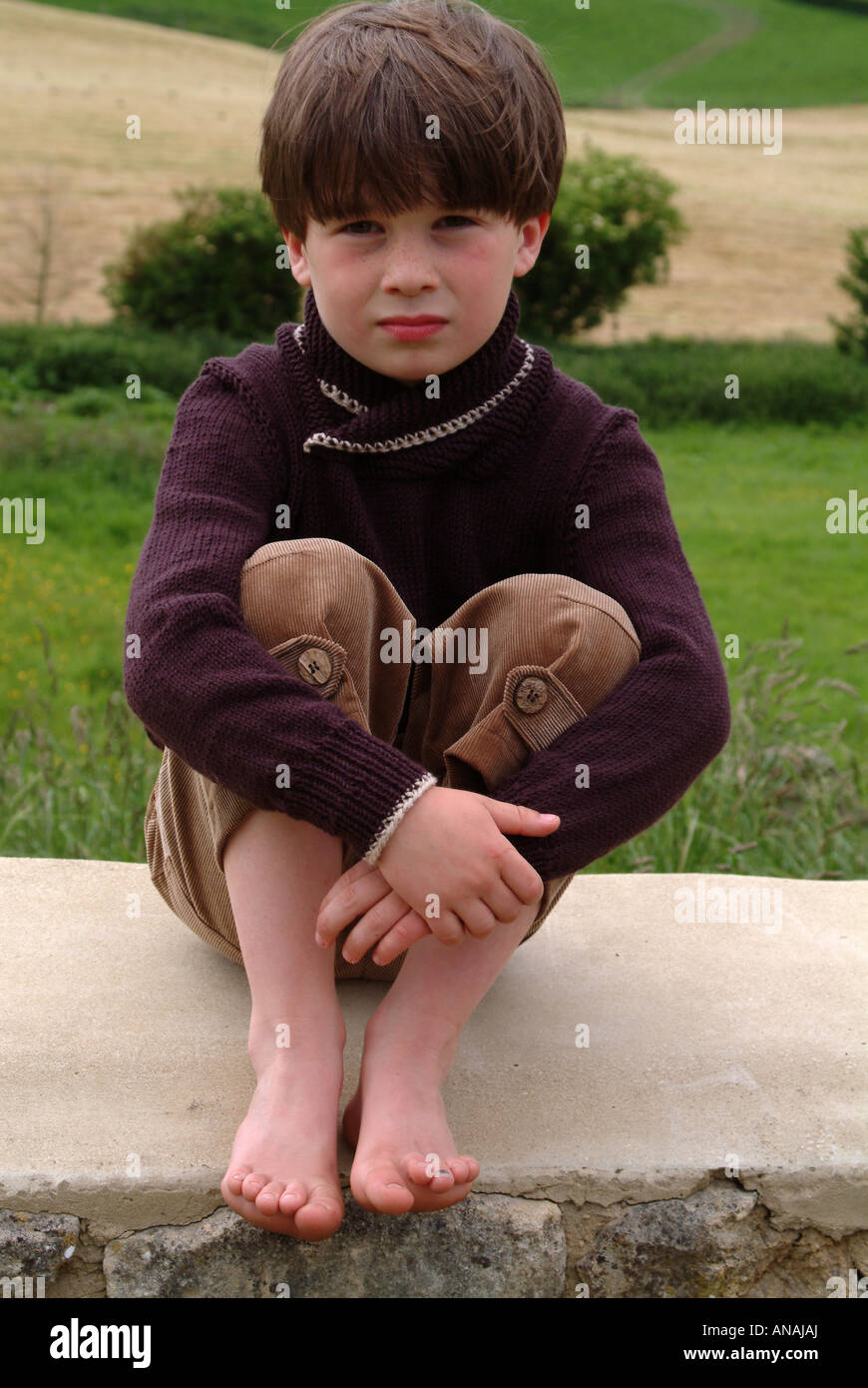 Ritratto di un ragazzino seduto su un muro di pietra cercando alimentato fino Foto Stock