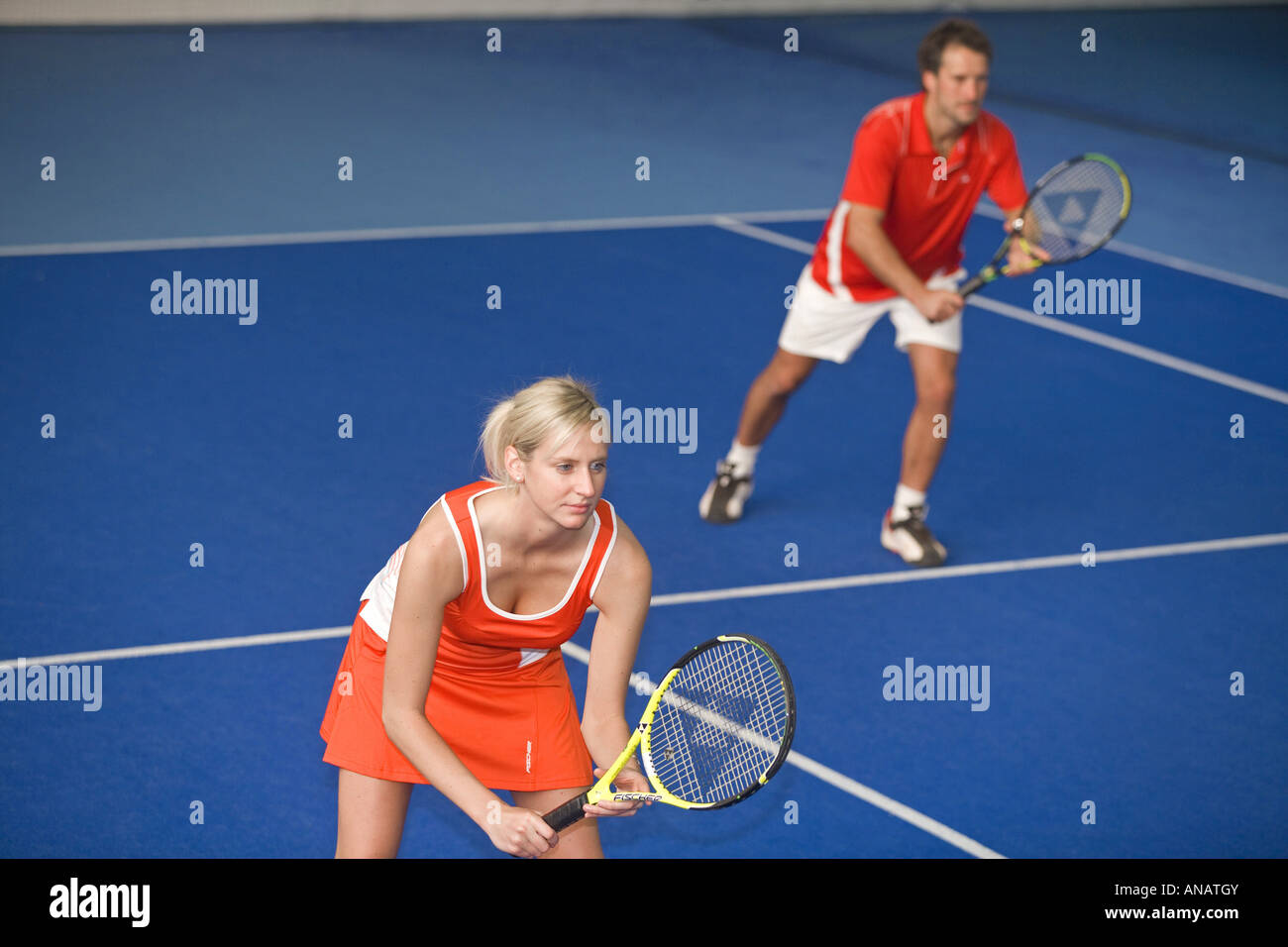 Matura in rosso sportswear giocando misti tennis doppio Foto Stock