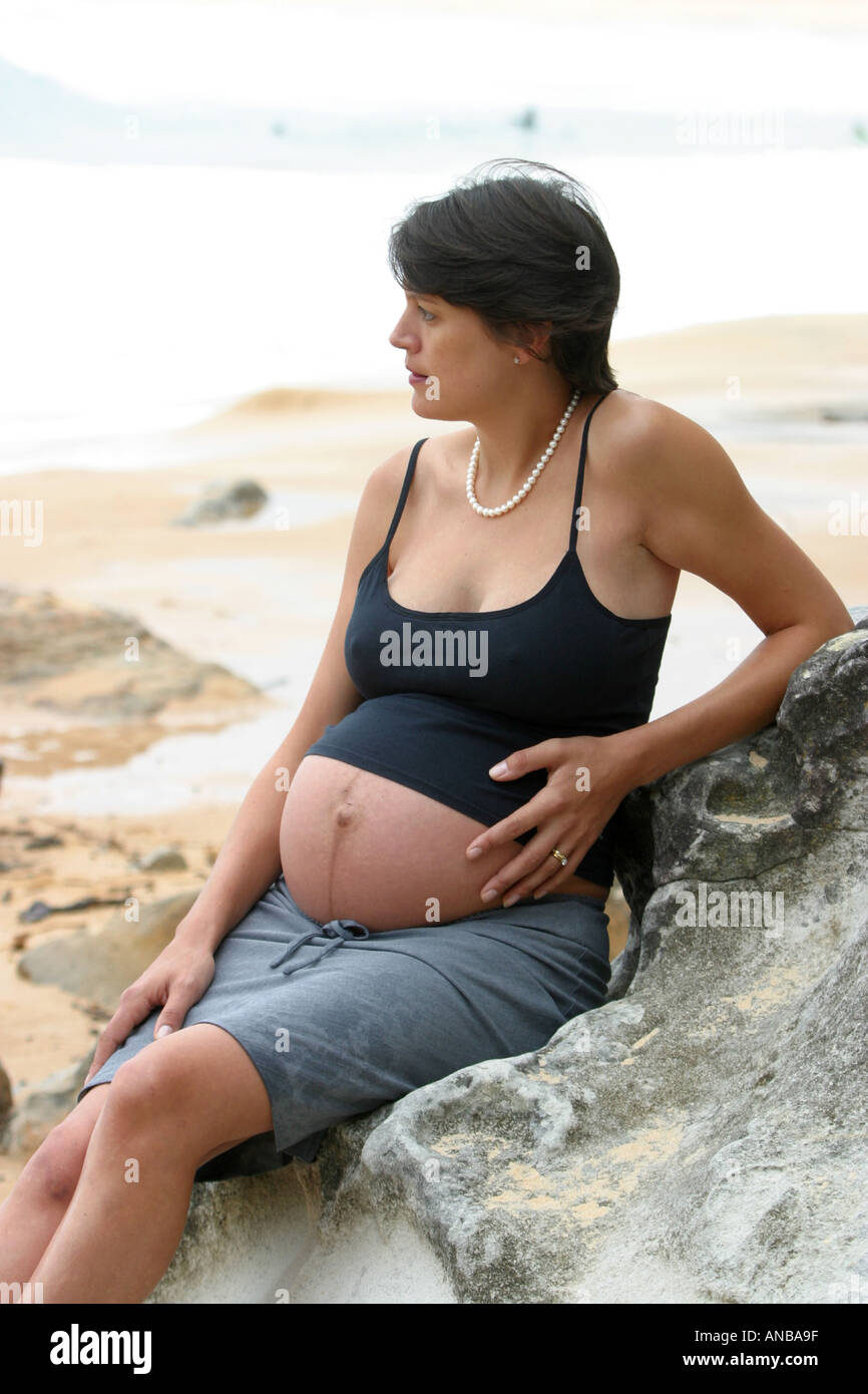 Donna incinta che indossa una metà superiore riff quasi pieno termine su una spiaggia da sé Foto Stock