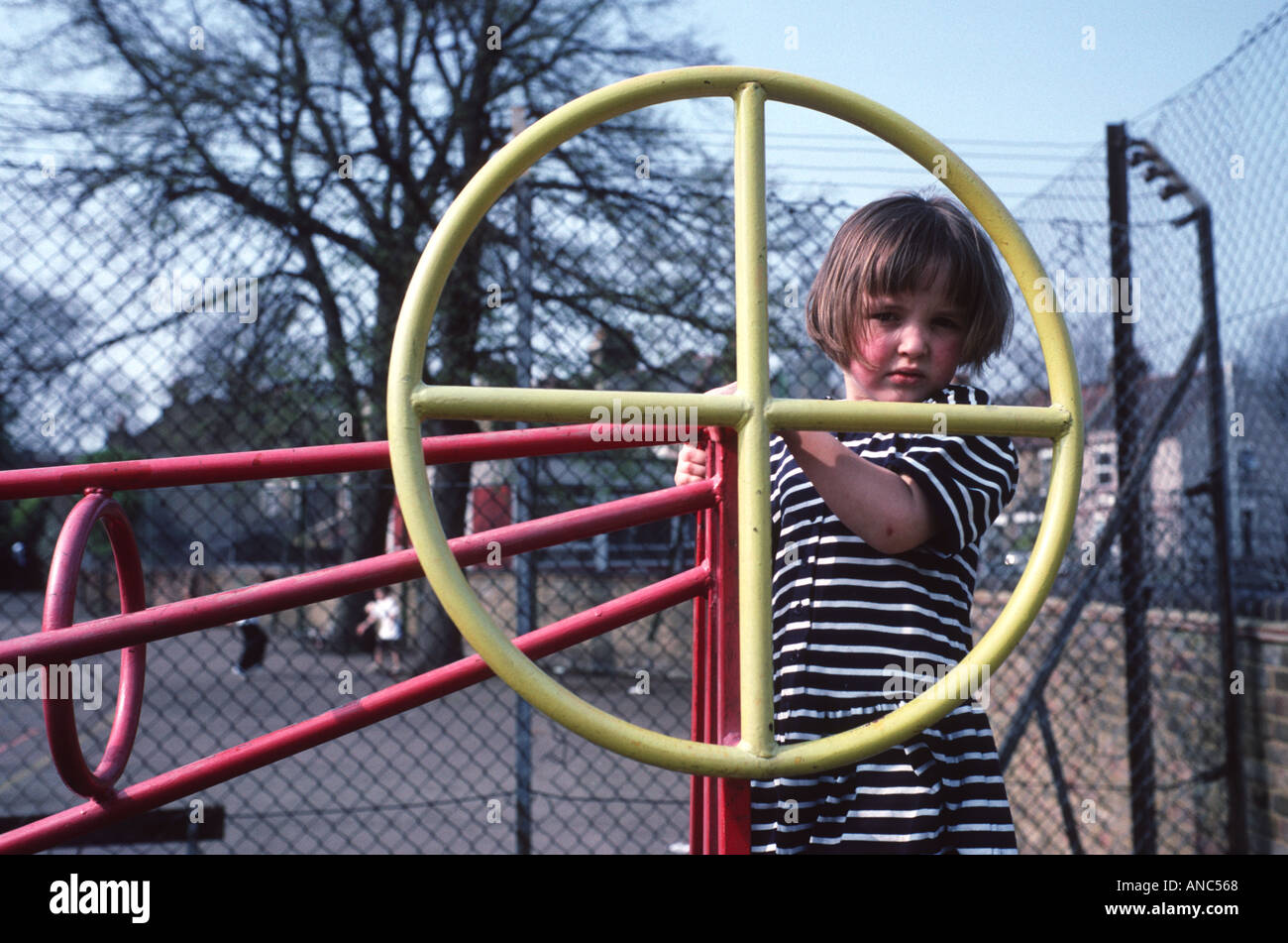 Grave alla ricerca di piccola ragazza cerca attraverso un rosso e giallo telaio di arrampicata a bambini Parco di oscillazione Foto Stock