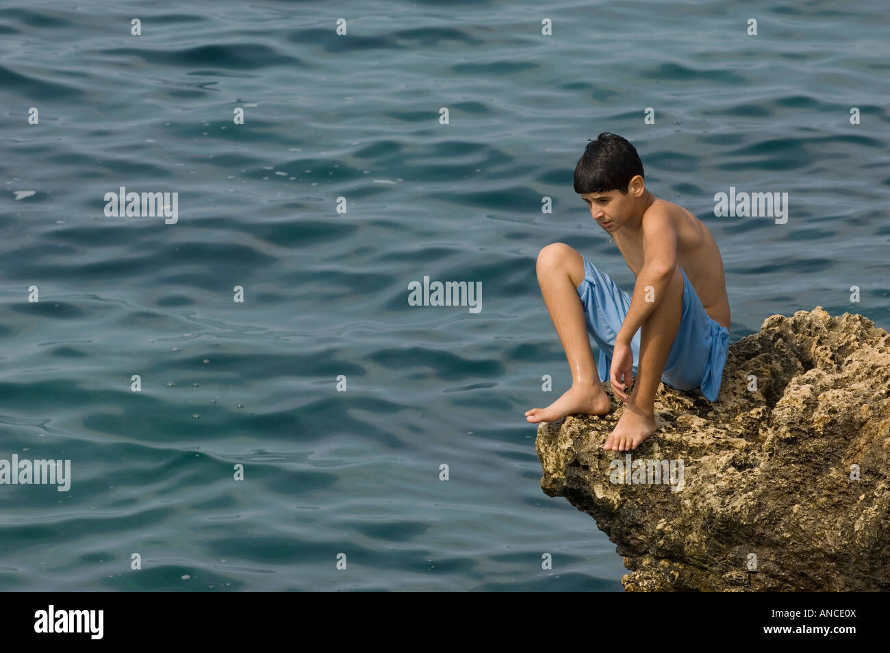 Ragazzo seduto sul bordo del rock in riva al mare Foto Stock