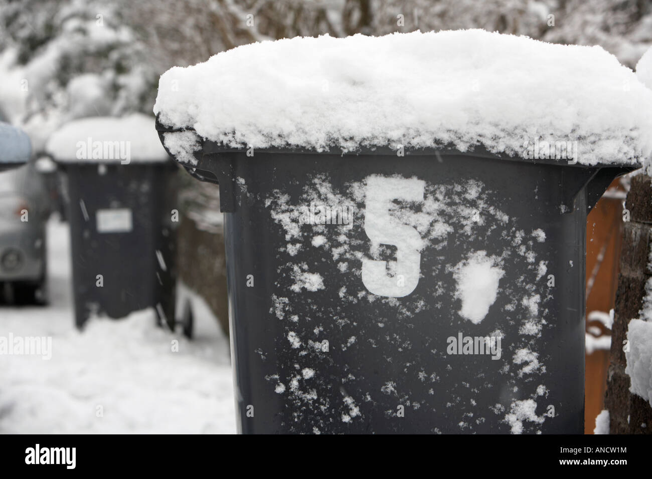 Rifiuti domestici rifiuti bidone con ruote con numero 5 ricoperta di neve seduti sulla strada Foto Stock