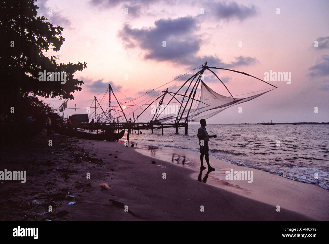 Cinese di reti da pesca sulla spiaggia al tramonto a Fort Cochin, Kerala Foto Stock