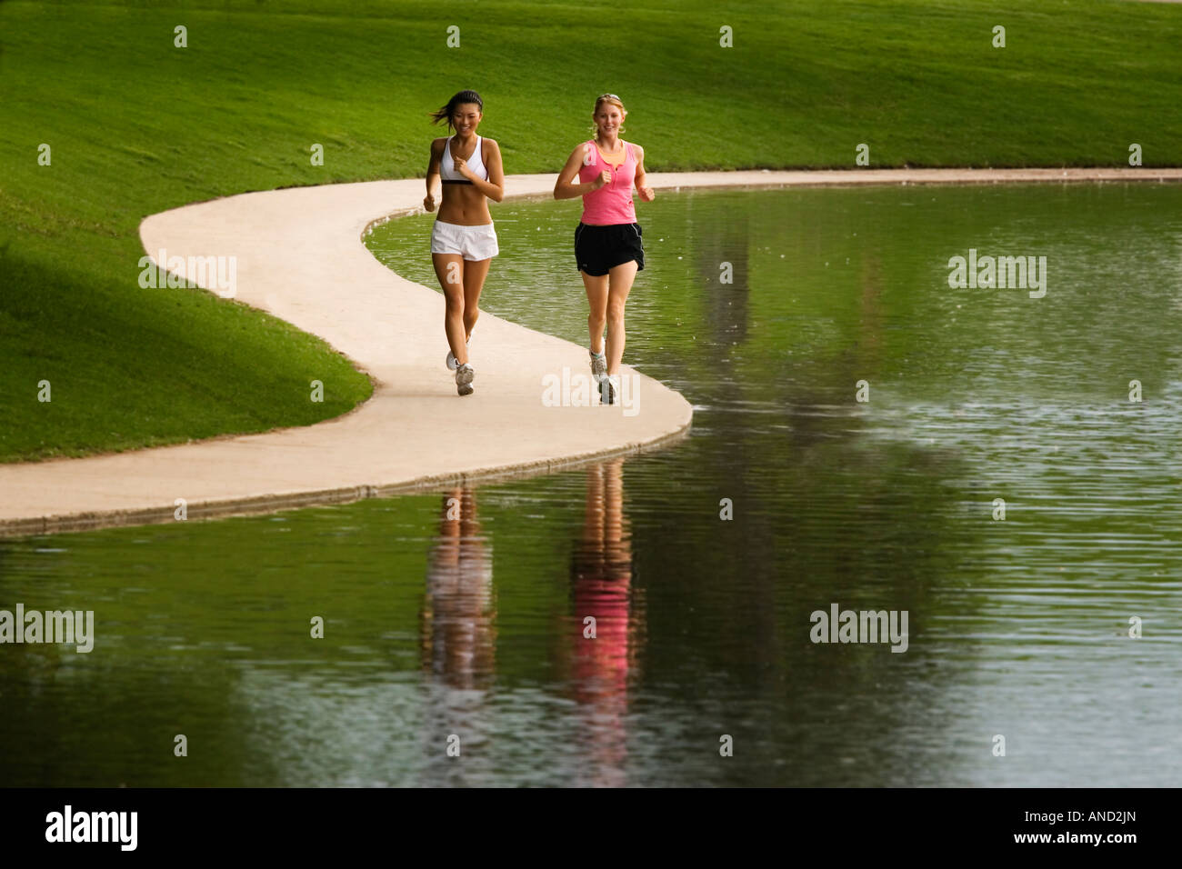 Due giovani donne asiatiche e caucasiche jogging accanto a un lago in un parco Foto Stock