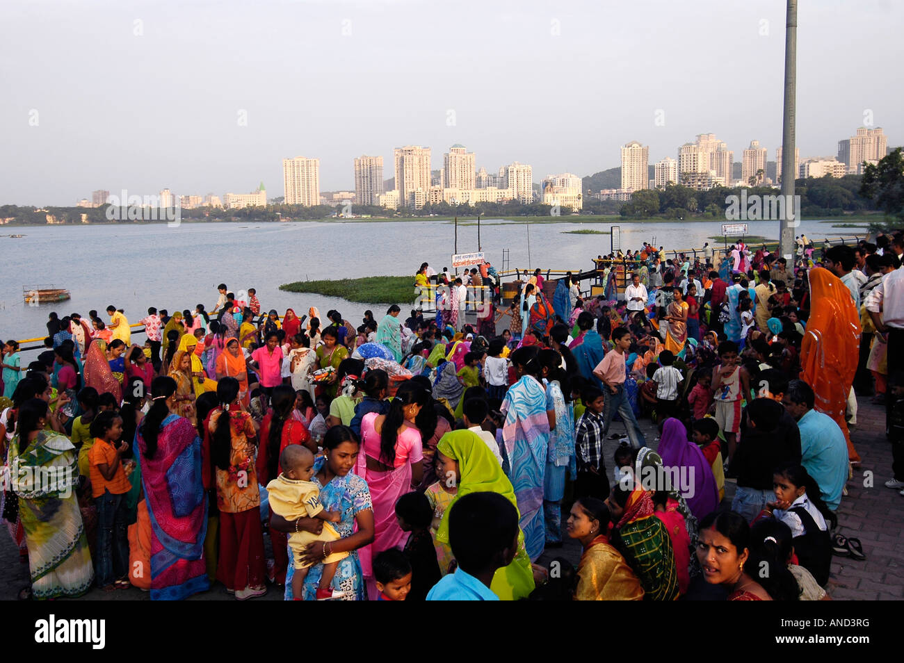 La folla di donne indiane e i bambini che frequentano un festival indù in prossimità di un lago in Mumbai, con grattacieli visibili in background. Foto Stock