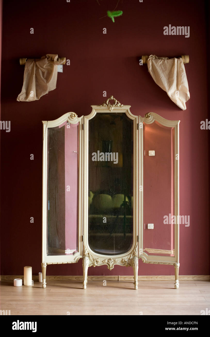 Specchio antico formata da tre pezzi situato in un basso camera illuminata con il bianco elegante tende a breve al di sopra Foto Stock