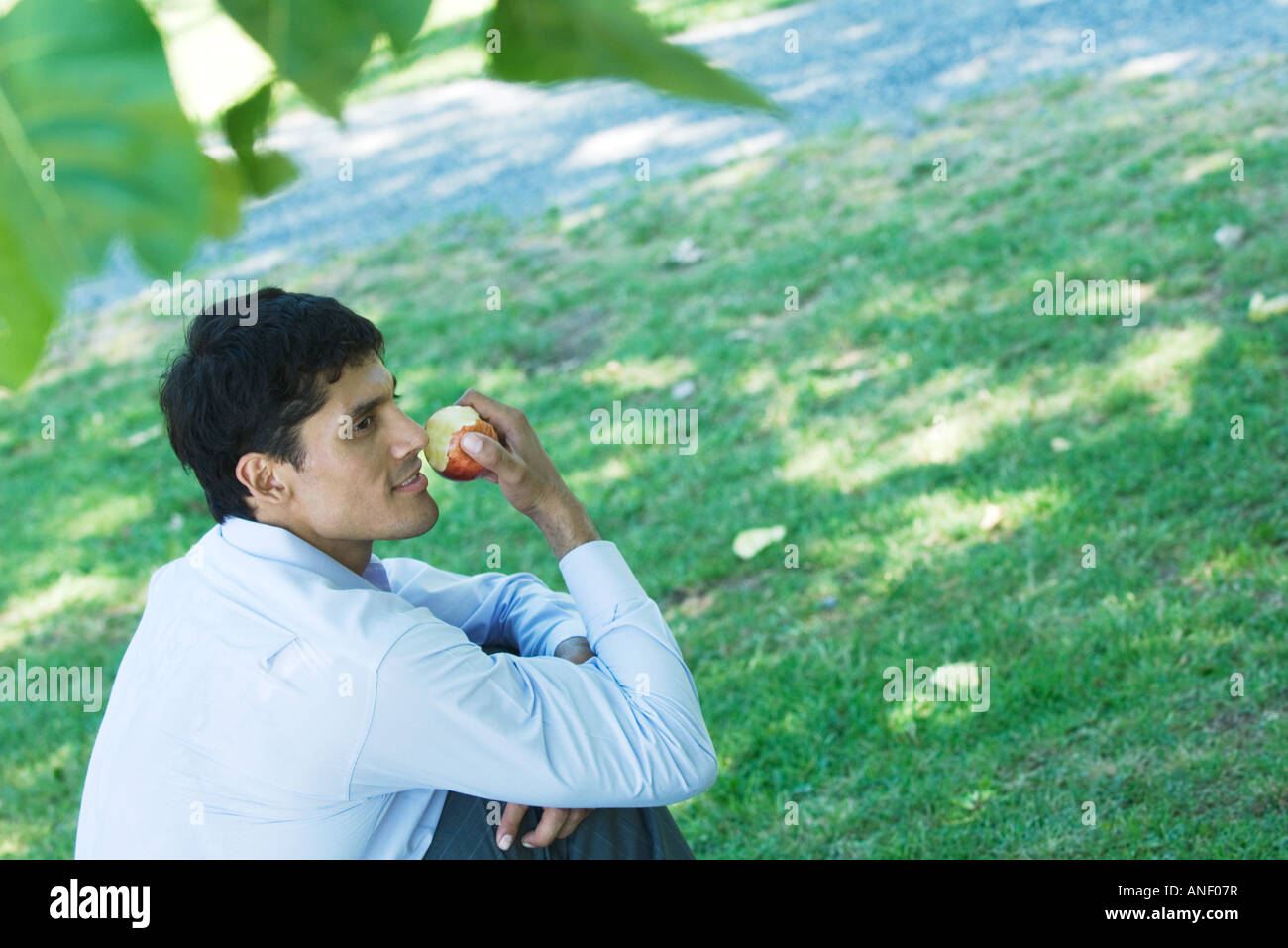 Imprenditore seduto sul terreno nel parco, mangiare apple Foto Stock