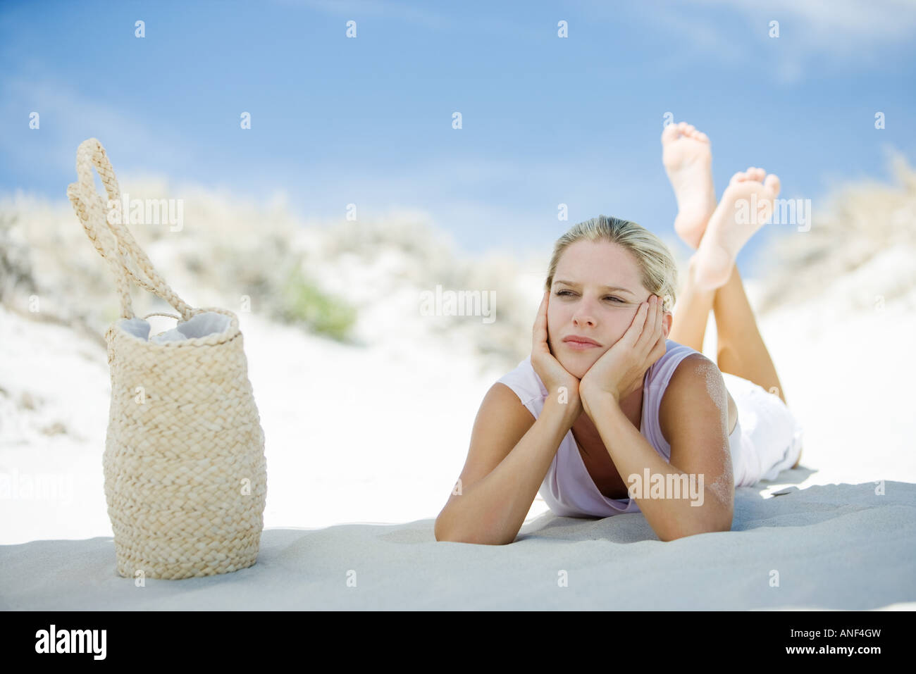 Giovane donna sdraiata sulla spiaggia, borsa da spiaggia nelle vicinanze Foto Stock