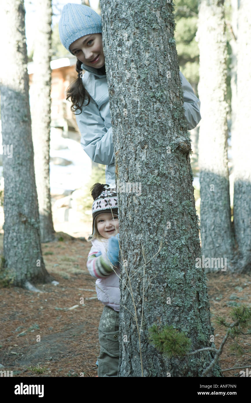 Teen ragazza e bambino, che spuntavano da dietro il tronco di albero Foto Stock