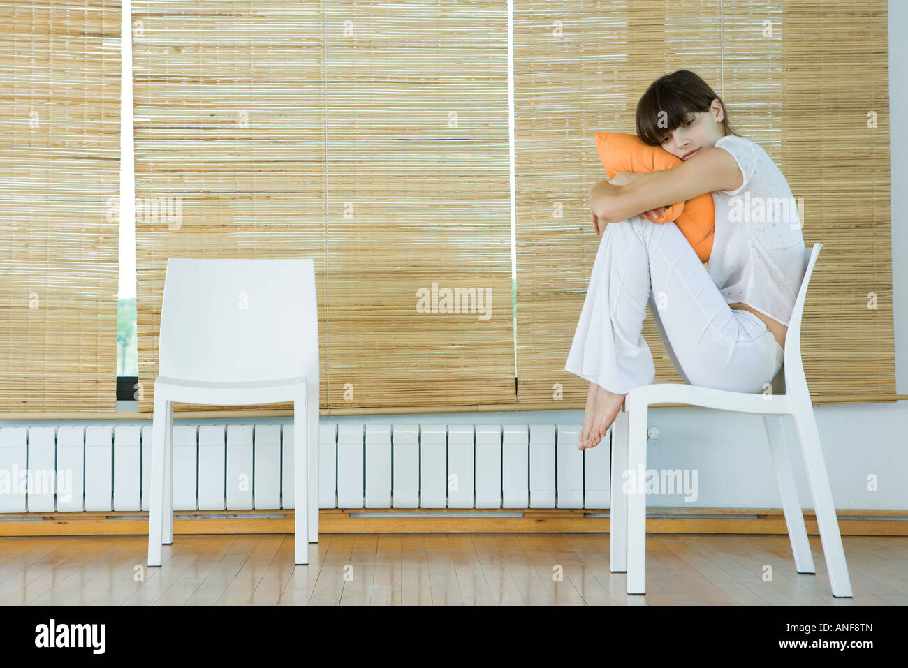 Giovane donna seduta in cattedra, abbracciando il cuscino Foto Stock