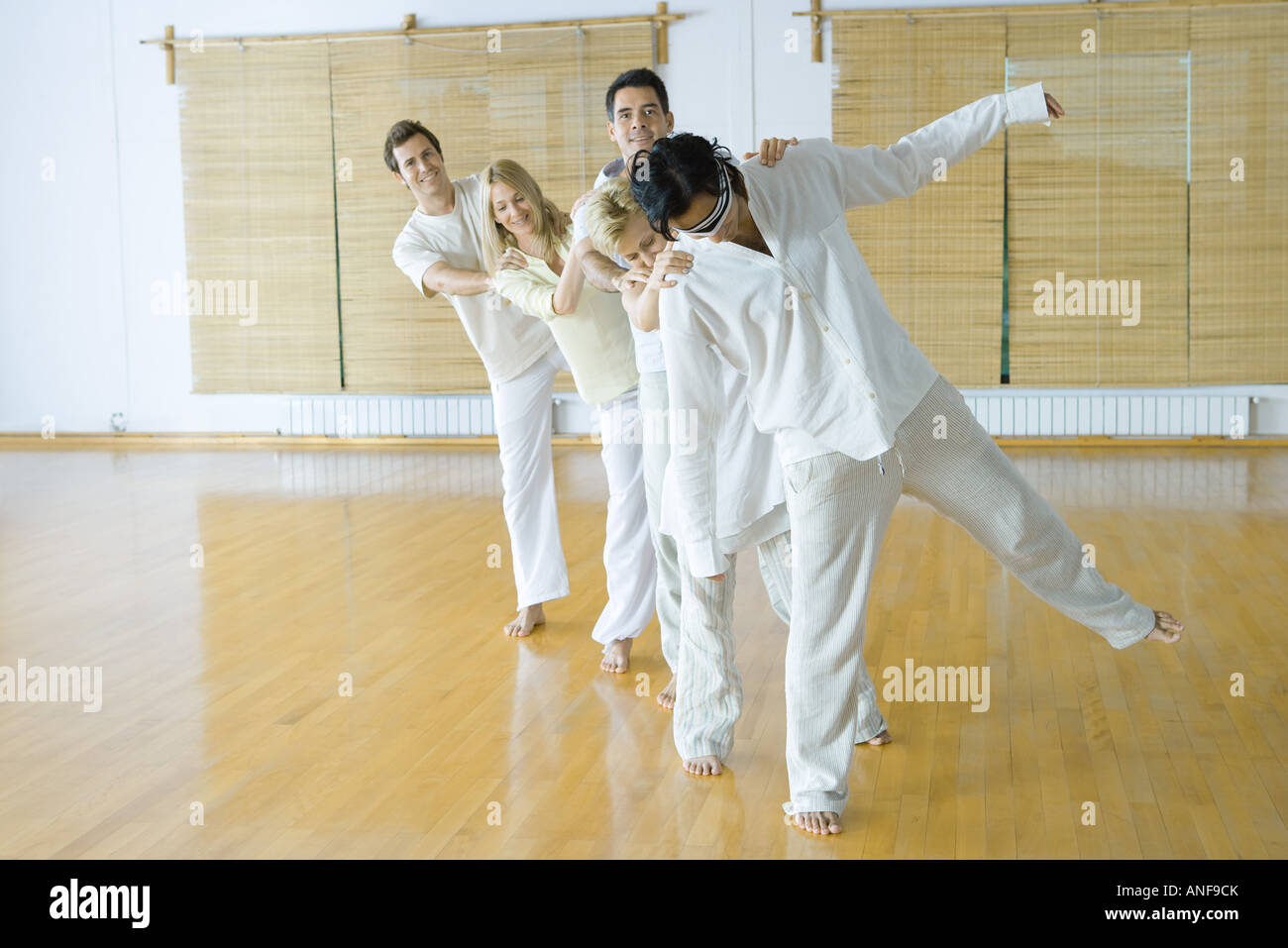 Gruppo di adulti in piedi solo file di tenere su ognuno alle spalle e gli occhi bendati leader sollevamento di una gamba in alto Foto Stock