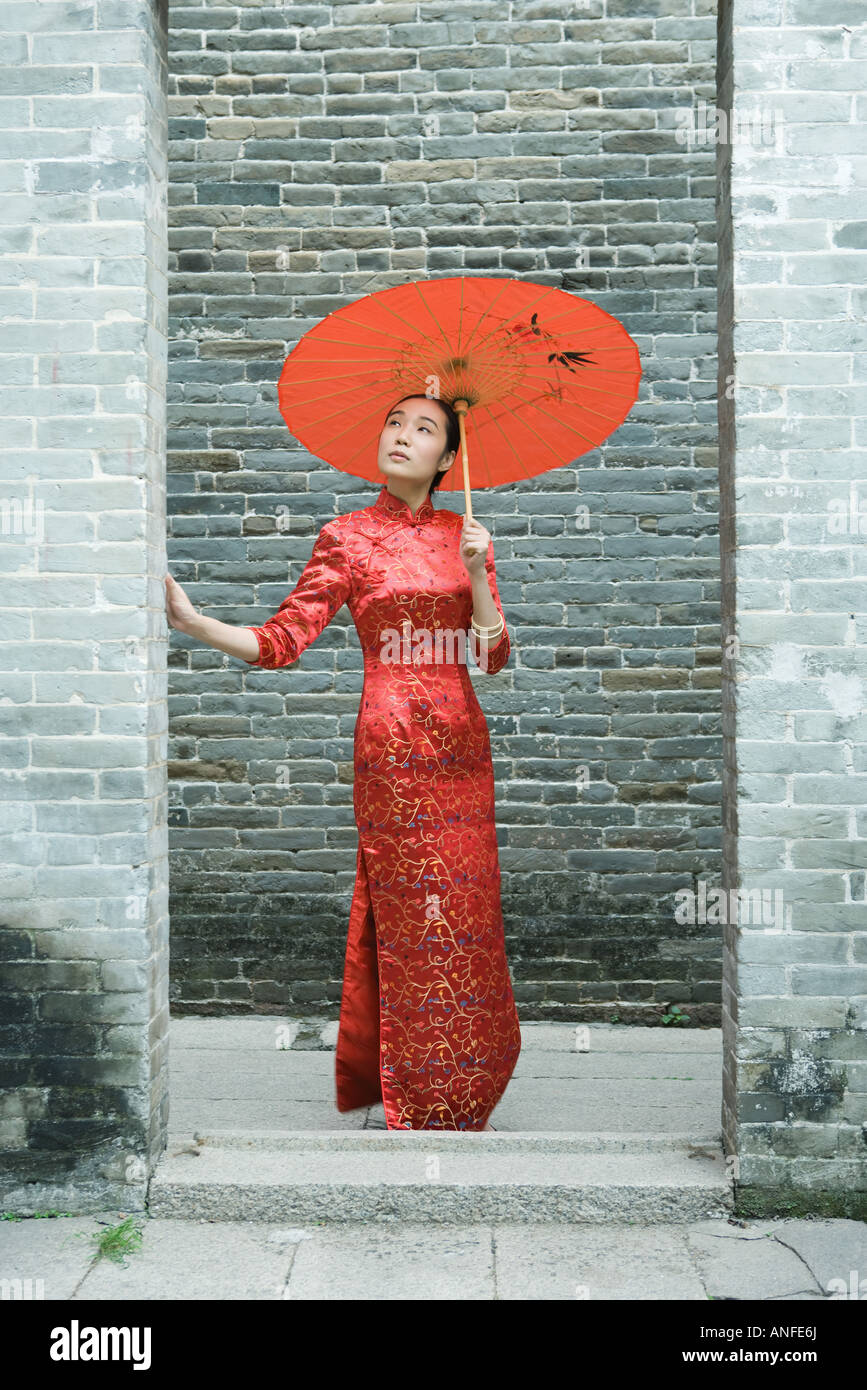 Giovane donna che indossa il cinese tradizionale abbigliamento, in piedi con ombrellone a piena lunghezza Foto Stock