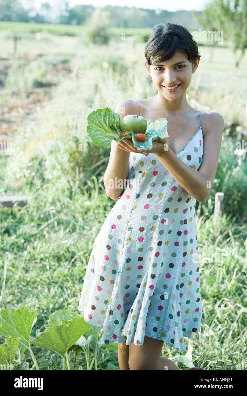 Giovane donna tenendo su prodotti freschi e di foglie di cavolo, sorridente in telecamera Foto Stock