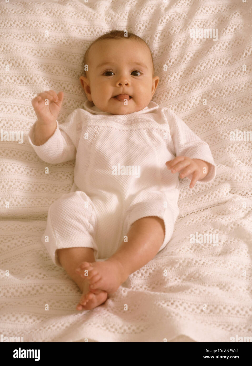 Cheeky baby ragazza distesa su un letto prendendo la sua lingua Foto Stock