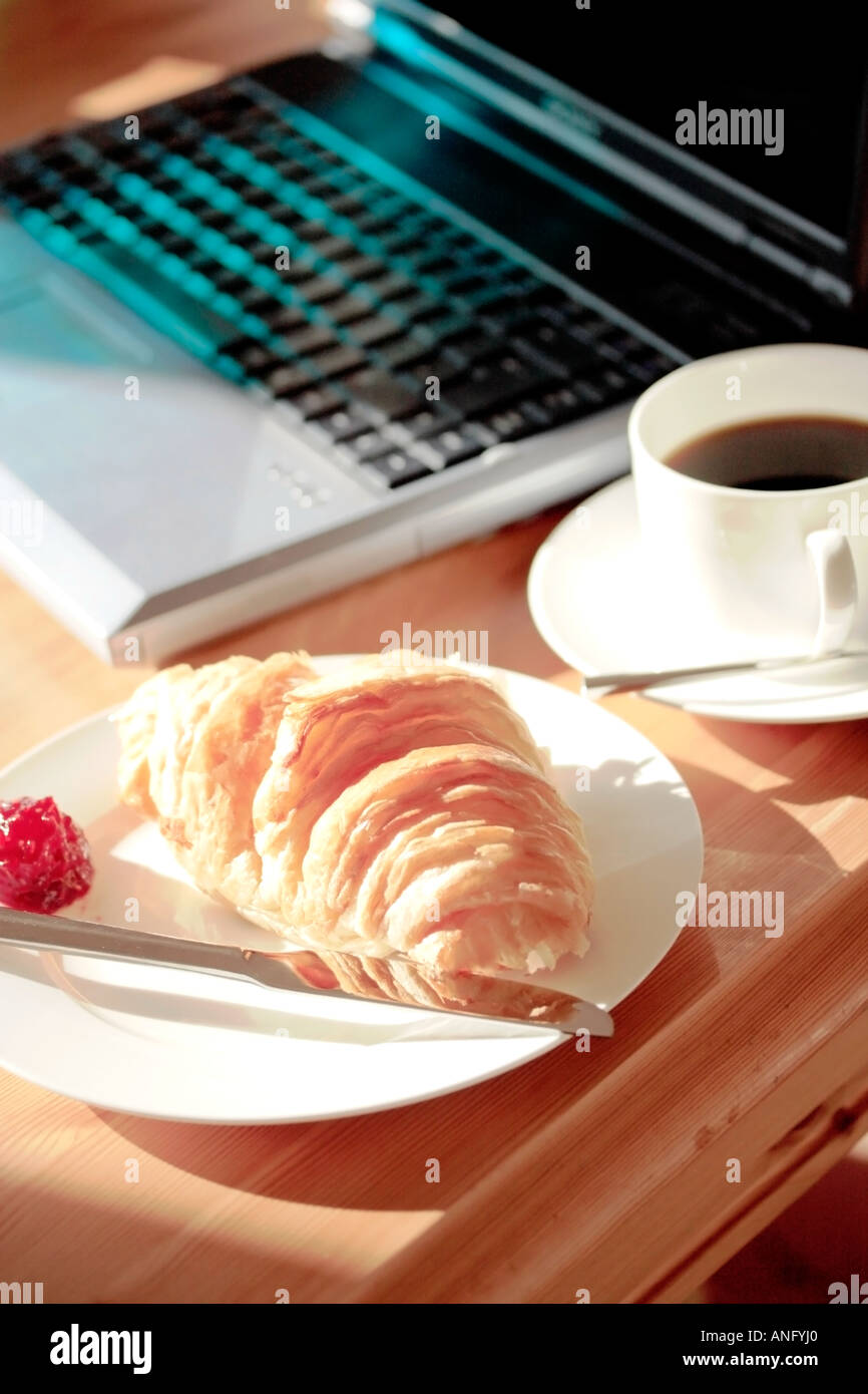 Close up di croissant e la tazza di caffè con il computer portatile nel sole mattutino Foto Stock