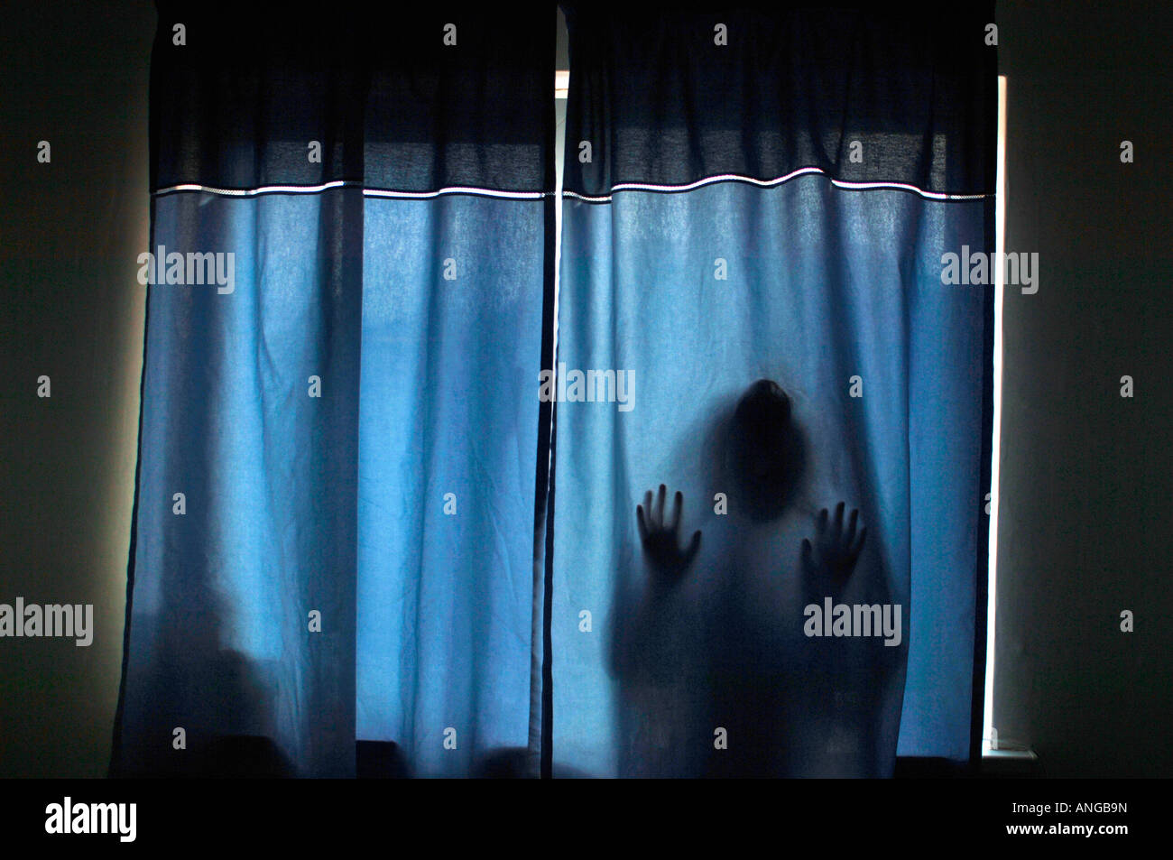 Un stagliano figura misteriosa, premendo contro tessuto blu tende. Foto Stock