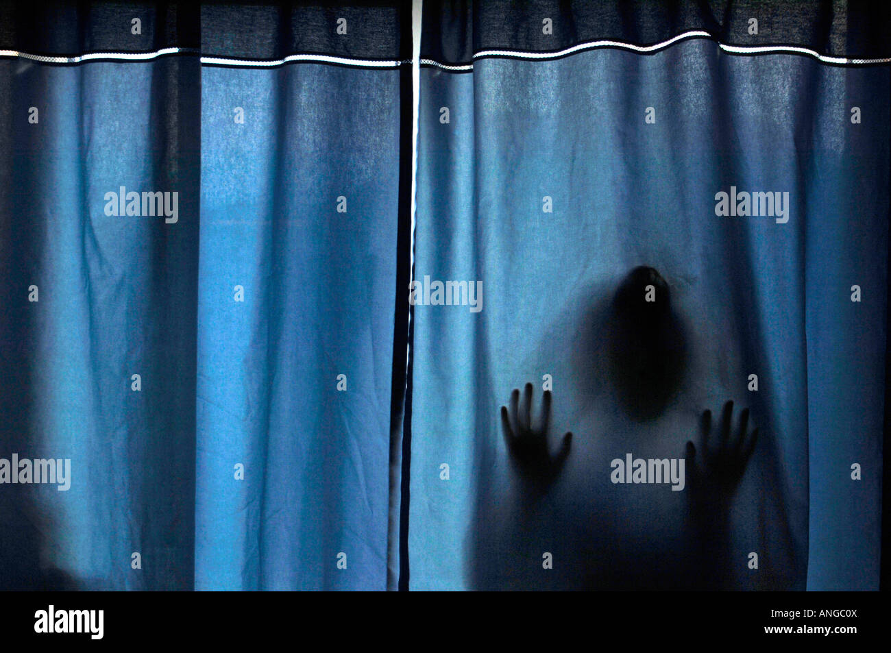 Un stagliano figura misteriosa, premendo contro tessuto blu tende. Foto Stock