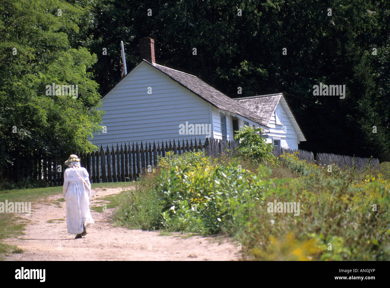 Lone ragazza nel lungo abito bianco con sun cofano a piedi una lunga countrypath pastorale alla sua fattoria rurale nella campagna Foto Stock