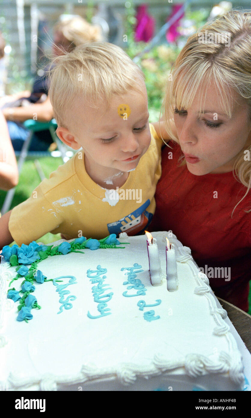 2 anno di età si brucia candele sulla torta di compleanno mentre viene trattenuta dalla sua madre Foto Stock