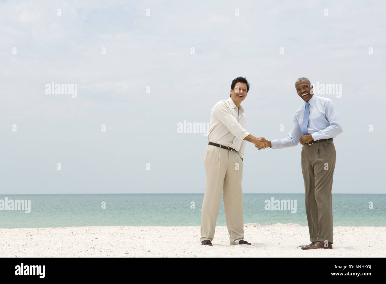Due imprenditori stringono le mani sulla spiaggia, entrambi sorridente in telecamera Foto Stock