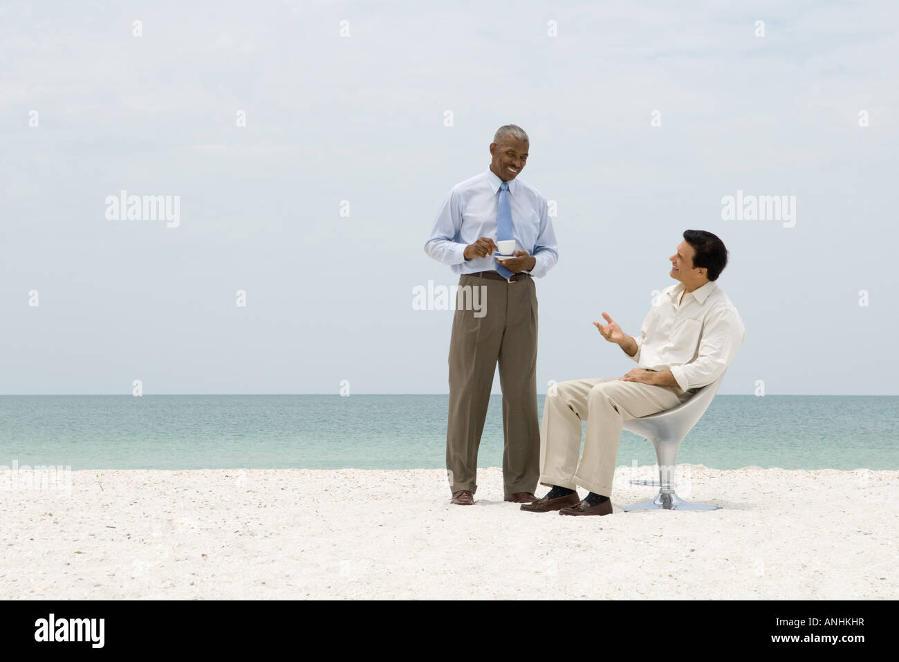 Due soci di affari in chat sulla spiaggia, una holding tazza da caffè Foto Stock