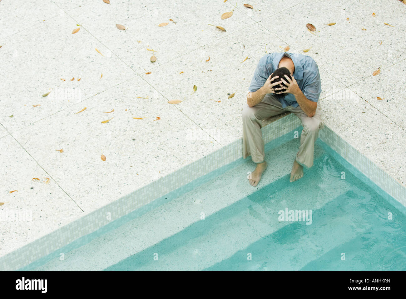 Uomo seduto con i piedi in piscina, tenendo testa, ad alto angolo di visione Foto Stock