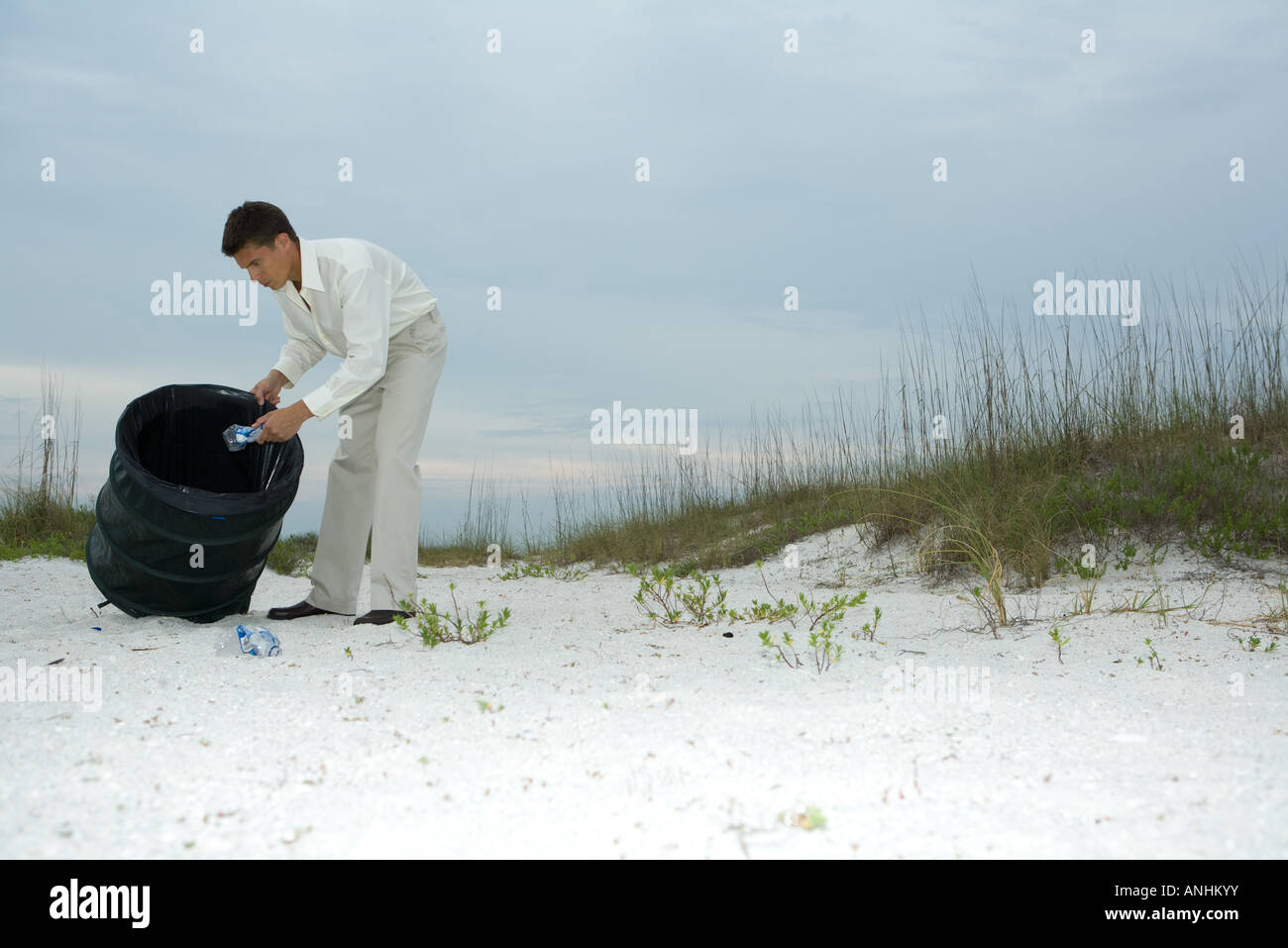 Uomo di scavare attraverso il cestino sulla spiaggia, rimozione di bottiglie in plastica Foto Stock