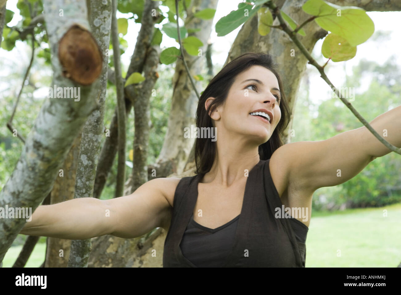 Donna tra alberi, sorridente, guardando lontano Foto Stock