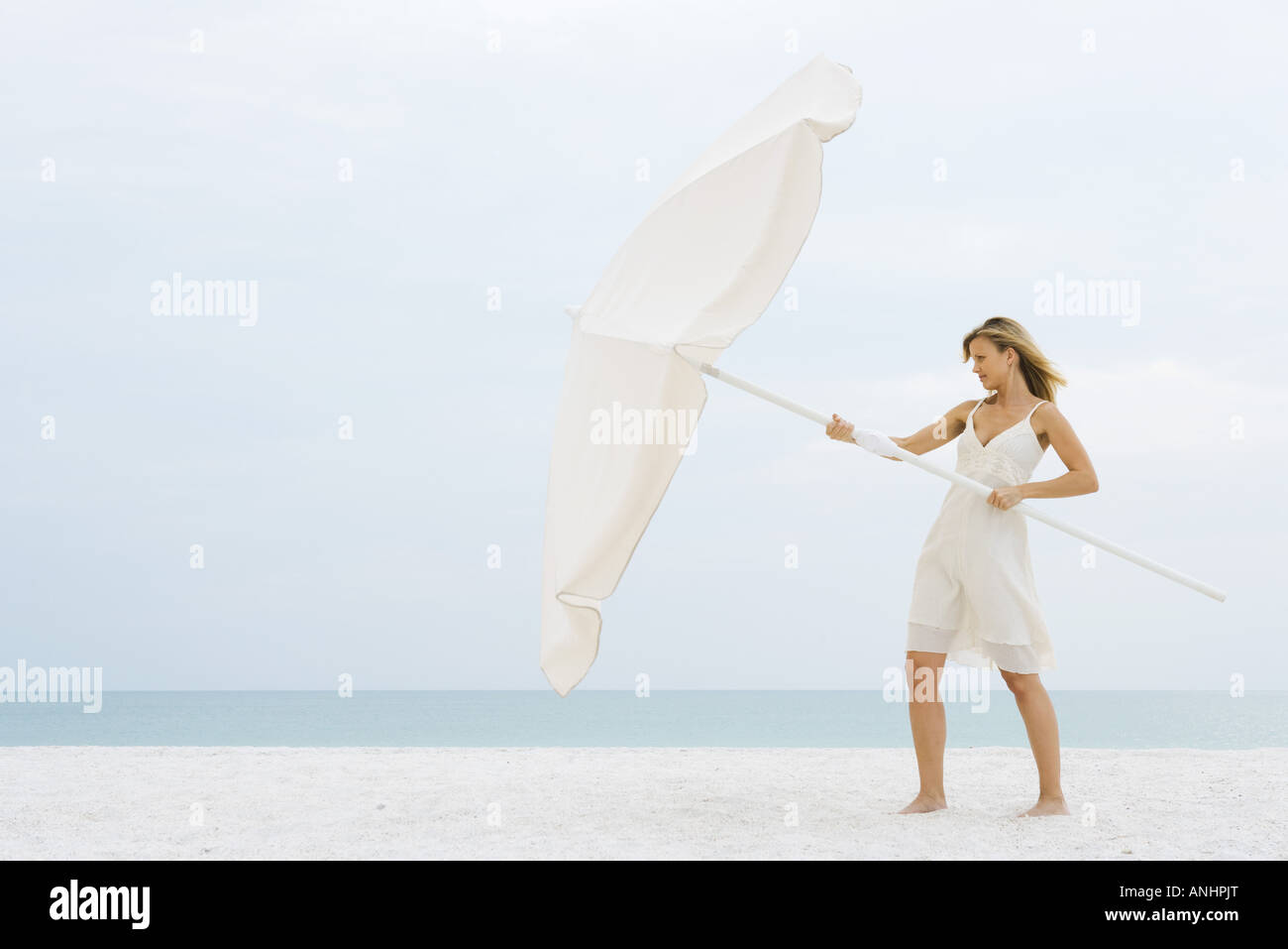Donna in piedi sulla spiaggia, l'apertura di grande ombrellone Foto Stock