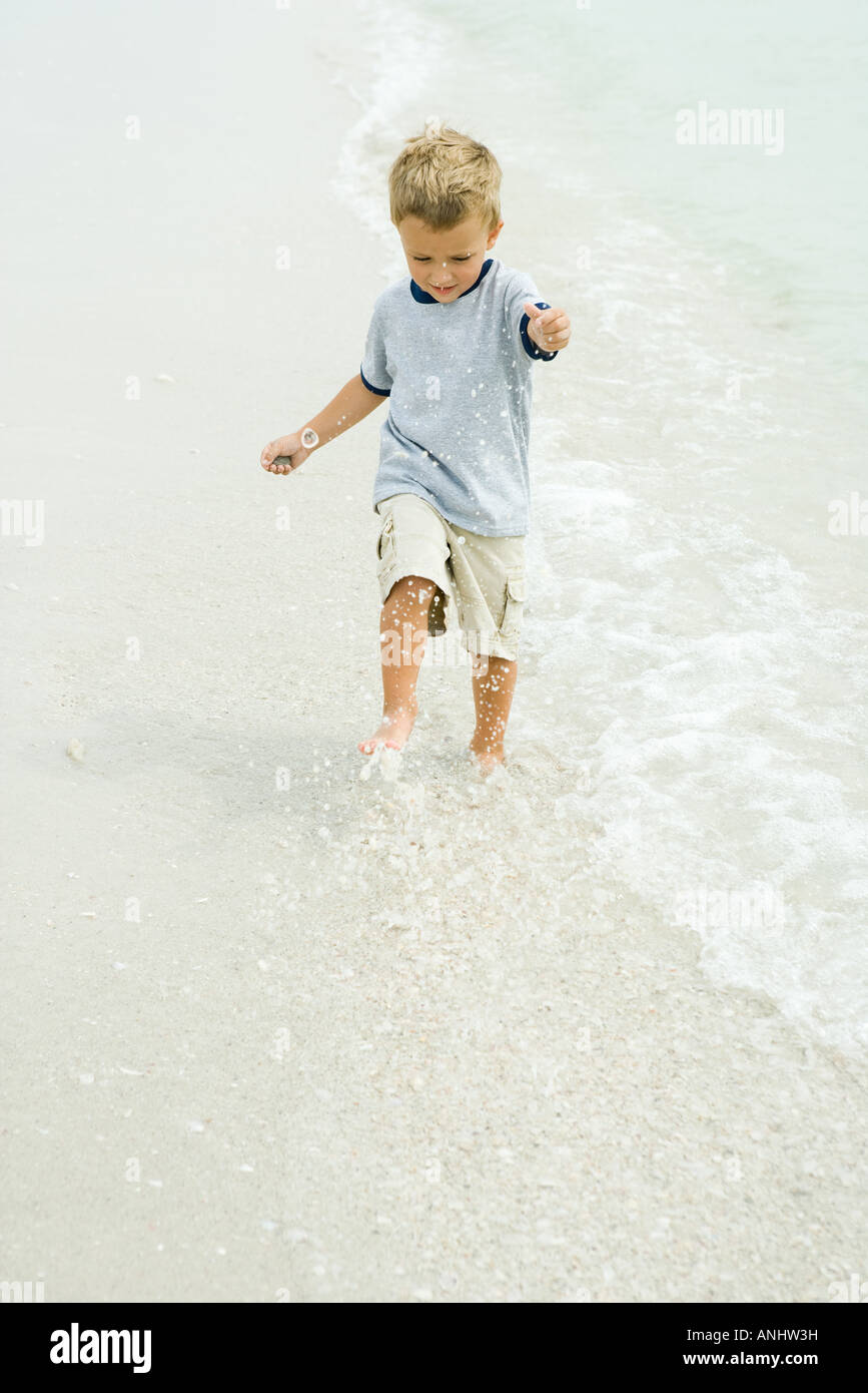 Little Boy spruzzi in surf sulla spiaggia a piena lunghezza Foto Stock
